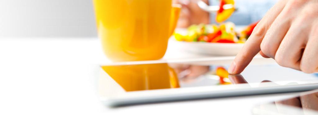 Man scrolling on tablet while eating vegetables with a yellow cup in front